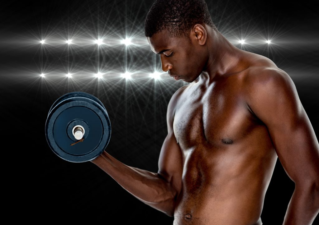 Muscular man working out with dumb bells against black background